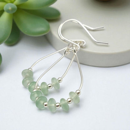 Green Crystal Sterling Silver Earrings featuring handmade dangle design with sea glass hoops, perfect for women who love unique statement jewelry. These artisanal earrings combine vibrant green crystals with delicate sterling silver craftsmanship, creating a stylish and eye-catching accessory. Ideal as a gift for her, they add a touch of natural elegance and boho flair to any outfit. Lightweight and versatile, these earrings are perfect for festivals, casual wear, or special occasions.