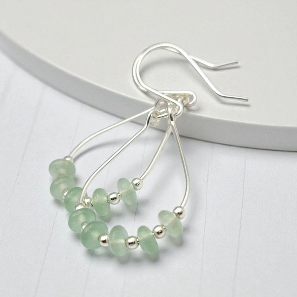 Green Crystal Sterling Silver Earrings featuring handmade dangle design with sea glass hoops, perfect for women who love unique statement jewelry. These artisanal earrings combine vibrant green crystals with delicate sterling silver craftsmanship, creating a stylish and eye-catching accessory. Ideal as a gift for her, they add a touch of natural elegance and boho flair to any outfit. Lightweight and versatile, these earrings are perfect for festivals, casual wear, or special occasions.