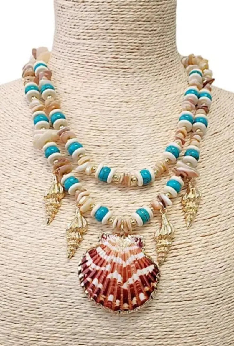 Layered seashell charm pendant necklace featuring blue, beige, and gold tones for a beachy boho look. This coastal jewelry piece captures ocean-inspired elegance with delicate shell charms and soft summer hues. Perfect for beach lovers and bohemian styles, it’s a thoughtful ocean-themed gift for her. Add a touch of seaside charm to your summer style with this lightweight, layered necklace that evokes the beauty of the coast