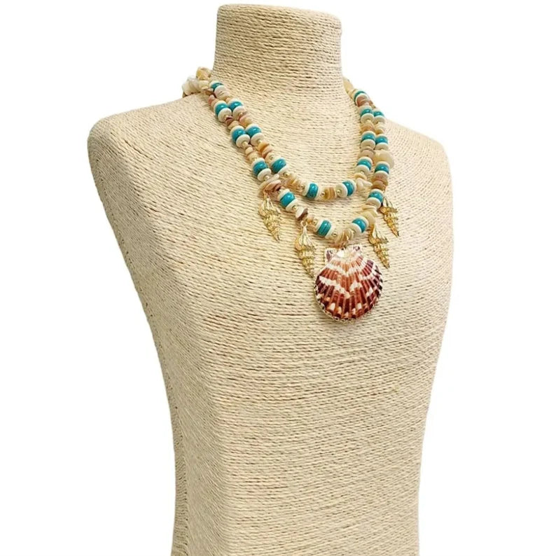 Layered seashell charm pendant necklace featuring blue, beige, and gold tones for a beachy boho look. This coastal jewelry piece captures ocean-inspired elegance with delicate shell charms and soft summer hues. Perfect for beach lovers and bohemian styles, it’s a thoughtful ocean-themed gift for her. Add a touch of seaside charm to your summer style with this lightweight, layered necklace that evokes the beauty of the coast