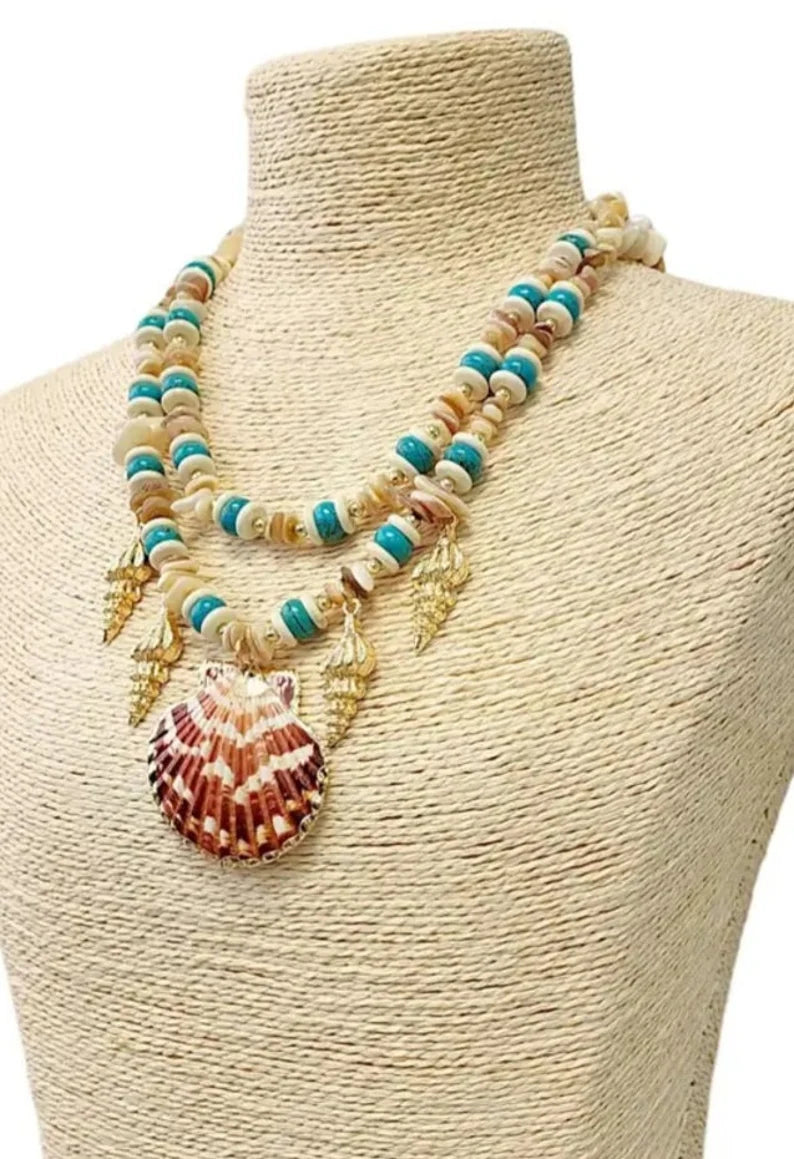 Layered seashell charm pendant necklace featuring blue, beige, and gold tones for a beachy boho look. This coastal jewelry piece captures ocean-inspired elegance with delicate shell charms and soft summer hues. Perfect for beach lovers and bohemian styles, it’s a thoughtful ocean-themed gift for her. Add a touch of seaside charm to your summer style with this lightweight, layered necklace that evokes the beauty of the coast