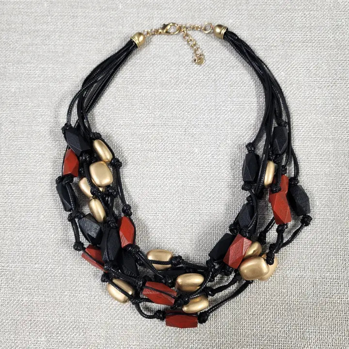 Red gold multi-strand necklace on black cord, featuring a bold boho statement design perfect for layered festival style. This handmade jewelry piece combines vibrant red gold tones with a sleek black cord, adding eye-catching contrast and texture. Ideal as a gift for her, it complements casual and festival outfits with effortless bohemian charm. A versatile accessory to elevate summer looks and outdoor gatherings