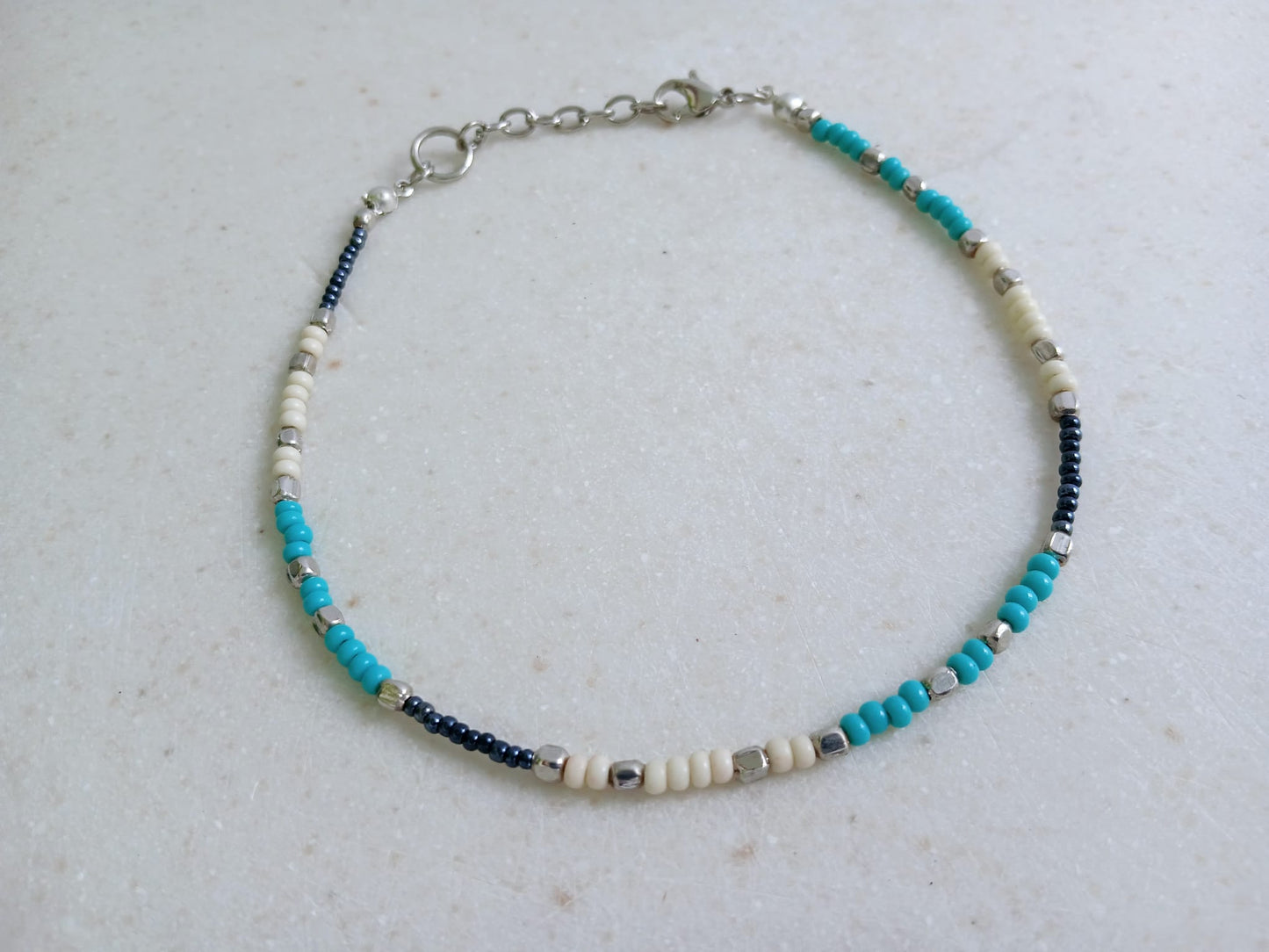 Cream Turquoise Beaded Anklet for Women featuring silver accent beads, handcrafted for a stylish boho beach vibe. This adjustable ankle bracelet blends natural cream and turquoise tones, making it a perfect summer foot accessory. Lightweight and comfortable, it's ideal for beachwear, festivals, or casual outfits. A thoughtful handmade gift for women who love bohemian jewelry and coastal-inspired fashion. Great for layering or wearing solo.