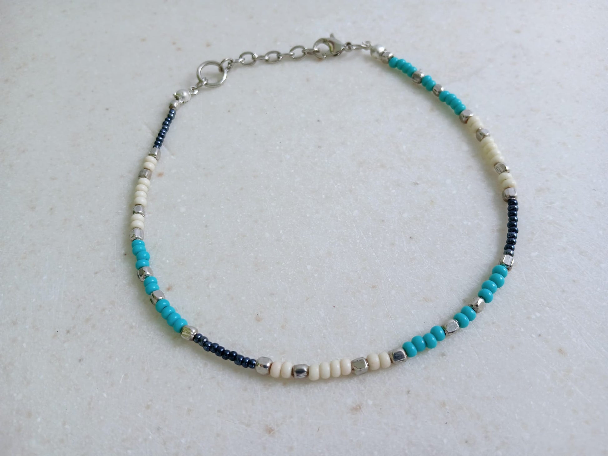 Cream Turquoise Beaded Anklet for Women featuring silver accent beads, handcrafted for a stylish boho beach vibe. This adjustable ankle bracelet blends natural cream and turquoise tones, making it a perfect summer foot accessory. Lightweight and comfortable, it's ideal for beachwear, festivals, or casual outfits. A thoughtful handmade gift for women who love bohemian jewelry and coastal-inspired fashion. Great for layering or wearing solo.