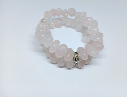 May include: A double-strand bracelet made of light pink rose quartz beads. The beads are smooth and oval-shaped. The bracelet has a silver clasp with small clear stones.