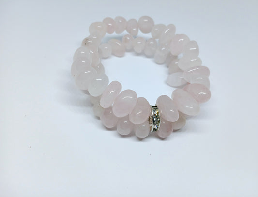 May include: A double-strand bracelet made of light pink rose quartz beads. The beads are smooth and oval-shaped. The bracelet has a silver clasp with small clear stones.