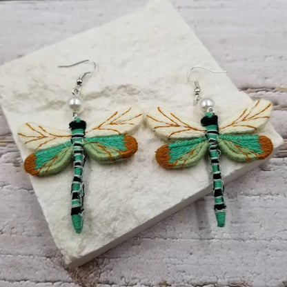 Fall vintage cloth dragonfly earrings featuring intricate fabric wings in earthy autumn tones. These boho statement earrings are perfect for the season, combining rustic charm with nature-inspired elegance. Lightweight and unique, they make a thoughtful fall gift for her. Celebrate autumn with handcrafted dragonfly jewelry that adds a whimsical touch to any outfit. Ideal for bohemian styles and nature lovers alike