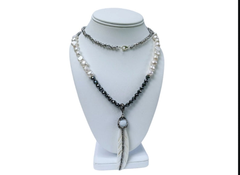 Hematite Mother of Pearl Necklace featuring a minimalist feather shell pendant, handcrafted into an elegant statement piece. This boho chic necklace combines the sleek, reflective hematite beads with the iridescent mother of pearl, creating a unique blend of natural beauty and modern style. Perfect as a gift for women who appreciate artisanal jewelry, it adds subtle sophistication and earthy charm to any outfit, ideal for both casual and formal occasions.