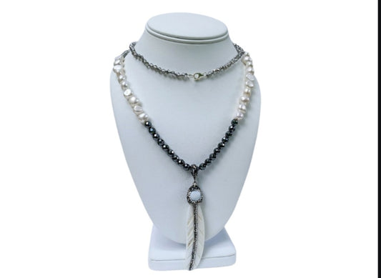 Hematite Mother of Pearl Necklace featuring a minimalist feather shell pendant, handcrafted into an elegant statement piece. This boho chic necklace combines the sleek, reflective hematite beads with the iridescent mother of pearl, creating a unique blend of natural beauty and modern style. Perfect as a gift for women who appreciate artisanal jewelry, it adds subtle sophistication and earthy charm to any outfit, ideal for both casual and formal occasions.