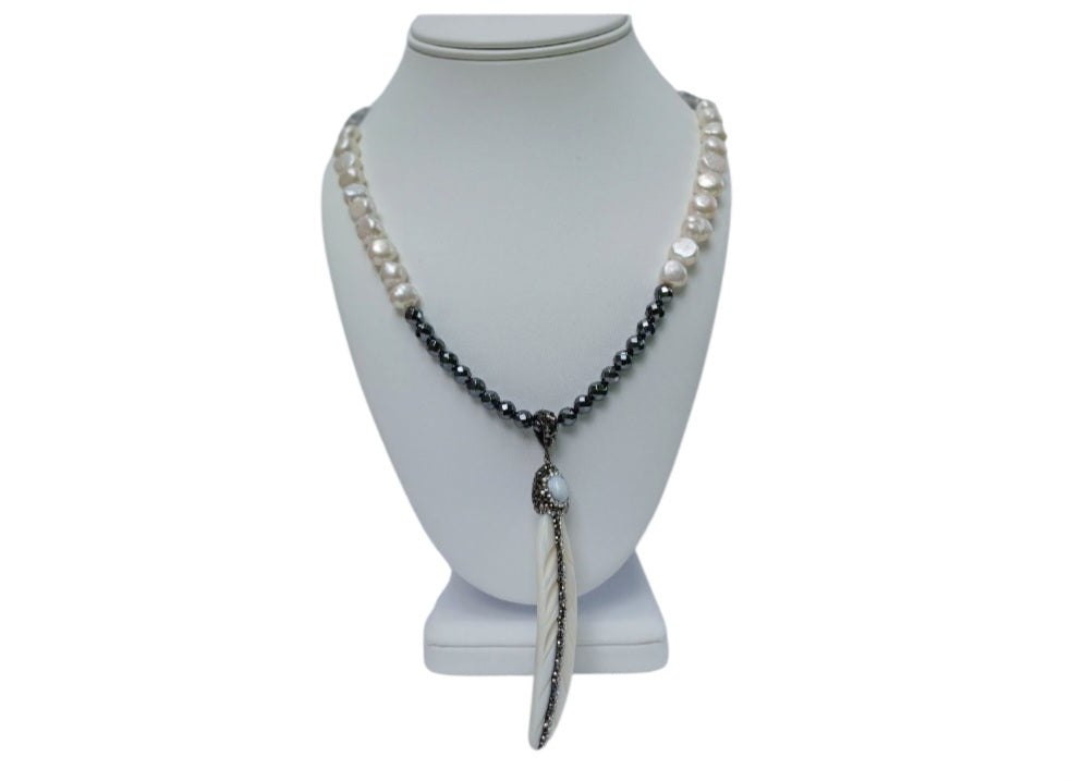 Hematite Mother of Pearl Necklace featuring a minimalist feather shell pendant, handcrafted into an elegant statement piece. This boho chic necklace combines the sleek, reflective hematite beads with the iridescent mother of pearl, creating a unique blend of natural beauty and modern style. Perfect as a gift for women who appreciate artisanal jewelry, it adds subtle sophistication and earthy charm to any outfit, ideal for both casual and formal occasions.