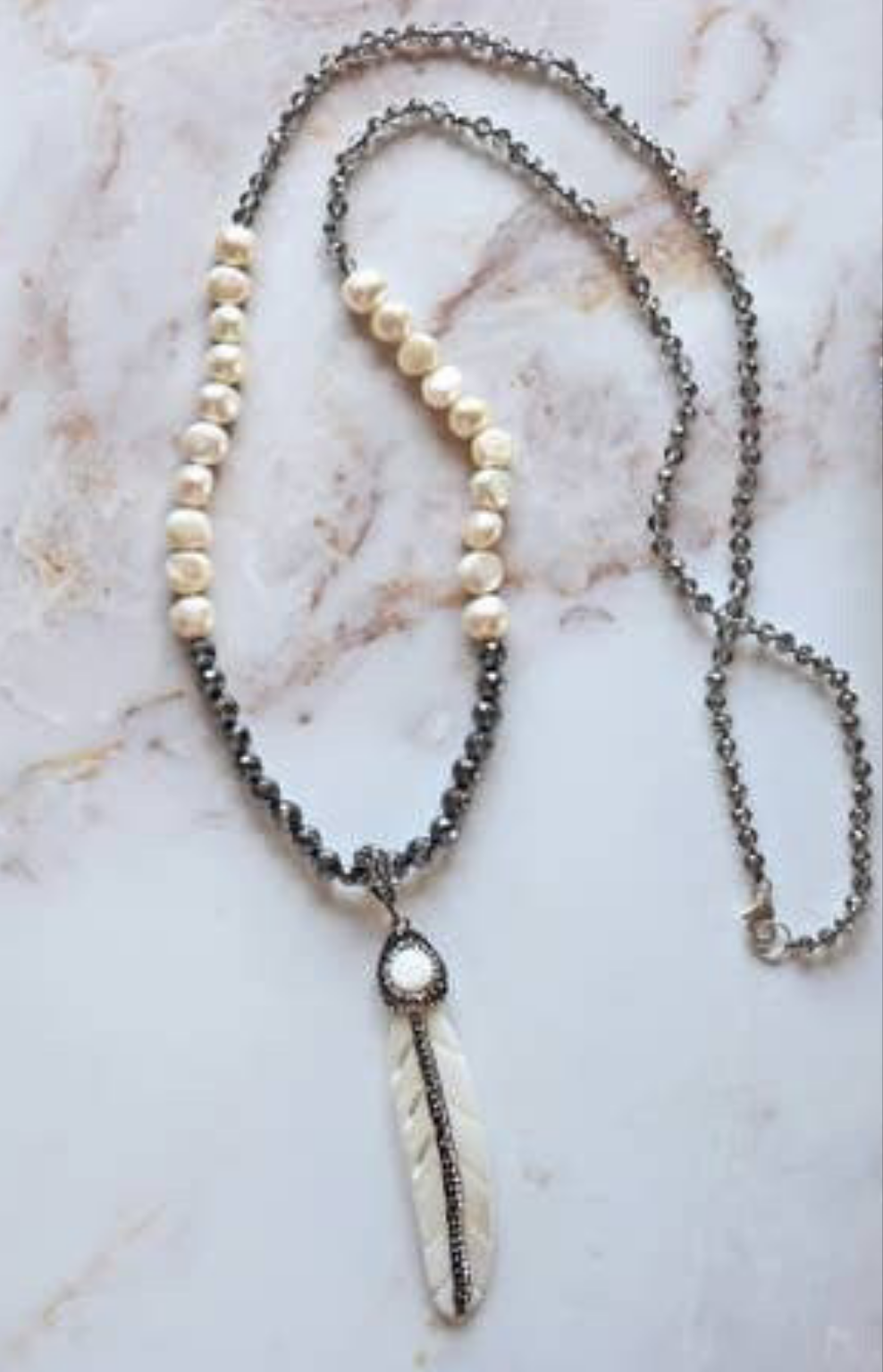 Hematite Mother of Pearl Necklace featuring a minimalist feather shell pendant, handcrafted into an elegant statement piece. This boho chic necklace combines the sleek, reflective hematite beads with the iridescent mother of pearl, creating a unique blend of natural beauty and modern style. Perfect as a gift for women who appreciate artisanal jewelry, it adds subtle sophistication and earthy charm to any outfit, ideal for both casual and formal occasions.