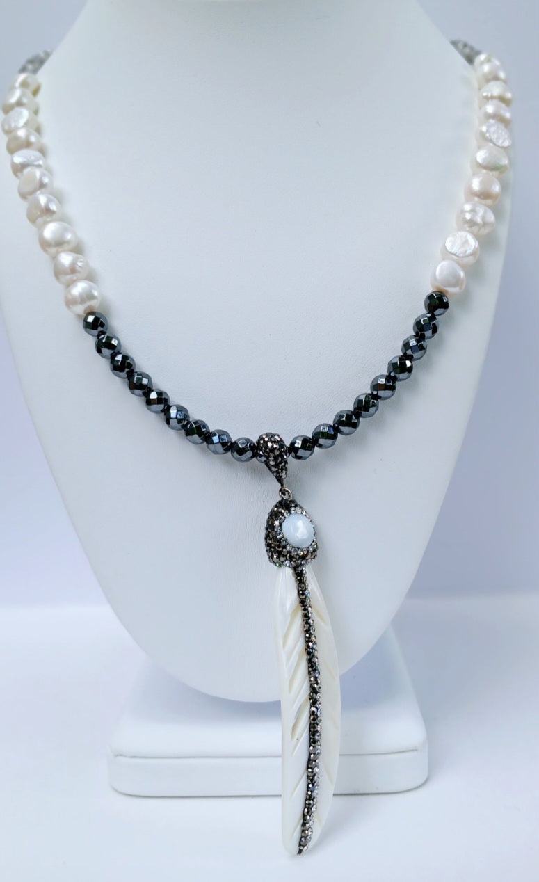 Hematite Mother of Pearl Necklace featuring a minimalist feather shell pendant, handcrafted into an elegant statement piece. This boho chic necklace combines the sleek, reflective hematite beads with the iridescent mother of pearl, creating a unique blend of natural beauty and modern style. Perfect as a gift for women who appreciate artisanal jewelry, it adds subtle sophistication and earthy charm to any outfit, ideal for both casual and formal occasions.