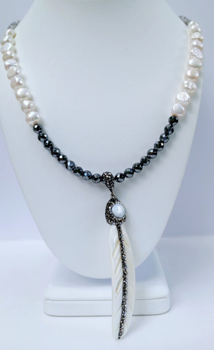 Hematite Mother of Pearl Necklace featuring a minimalist feather shell pendant, handcrafted into an elegant statement piece. This boho chic necklace combines the sleek, reflective hematite beads with the iridescent mother of pearl, creating a unique blend of natural beauty and modern style. Perfect as a gift for women who appreciate artisanal jewelry, it adds subtle sophistication and earthy charm to any outfit, ideal for both casual and formal occasions.