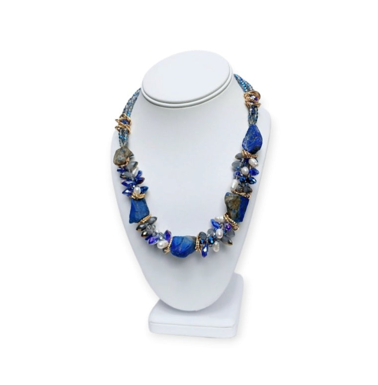 May include: A necklace made of blue and white stones with gold accents. The necklace is made of large, irregular shaped stones. The stones are strung together with gold wire. The necklace is displayed on a white mannequin.