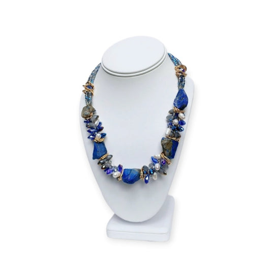 May include: A necklace made of blue and white stones with gold accents. The necklace is made of large, irregular shaped stones. The stones are strung together with gold wire. The necklace is displayed on a white mannequin.