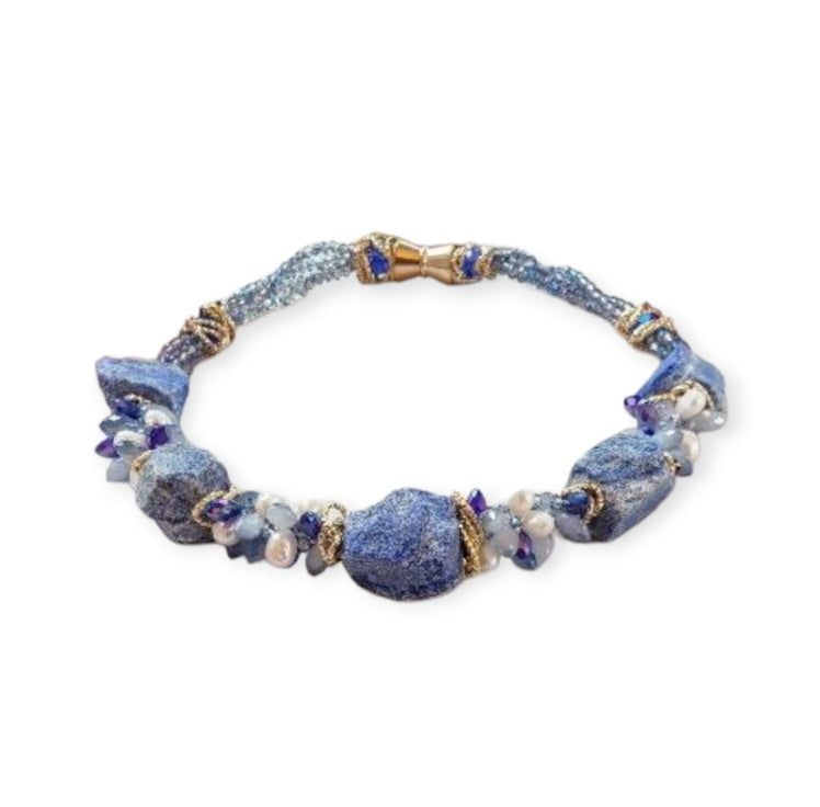 May include: A necklace made of blue and white stones with gold accents. The necklace is made of large, irregular shaped stones. The stones are strung together with gold wire. The necklace is displayed on a white mannequin.