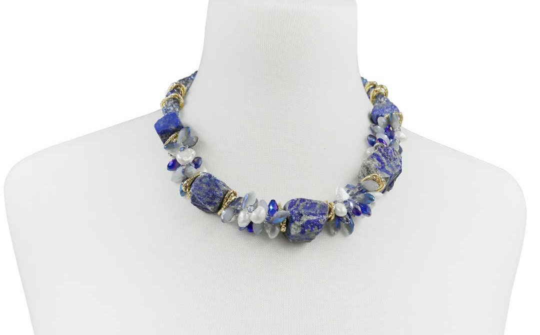 May include: A necklace made of blue and white stones with gold accents. The necklace is made of large, irregular shaped stones. The stones are strung together with gold wire. The necklace is displayed on a white mannequin.