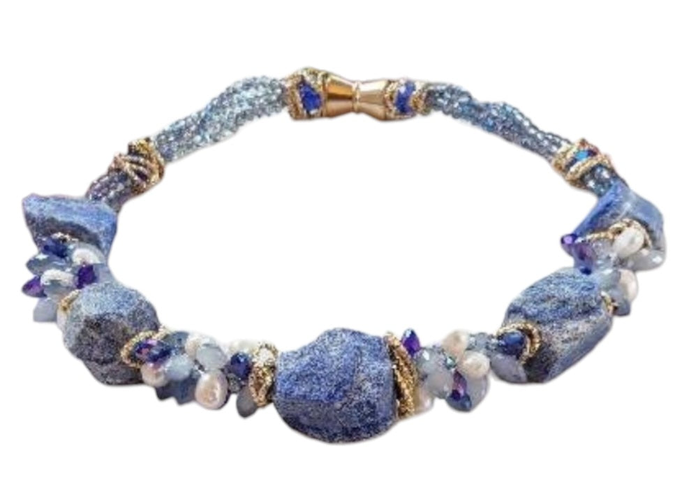 May include: A necklace made of blue and white stones with gold accents. The necklace is made of large, irregular shaped stones. The stones are strung together with gold wire. The necklace is displayed on a white mannequin.