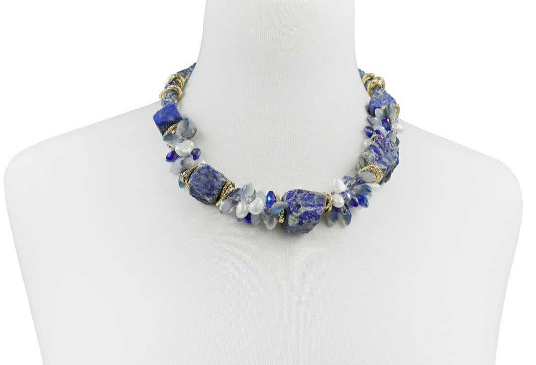 May include: A necklace made of blue and white stones with gold accents. The necklace is made of large, irregular shaped stones. The stones are strung together with gold wire. The necklace is displayed on a white mannequin.