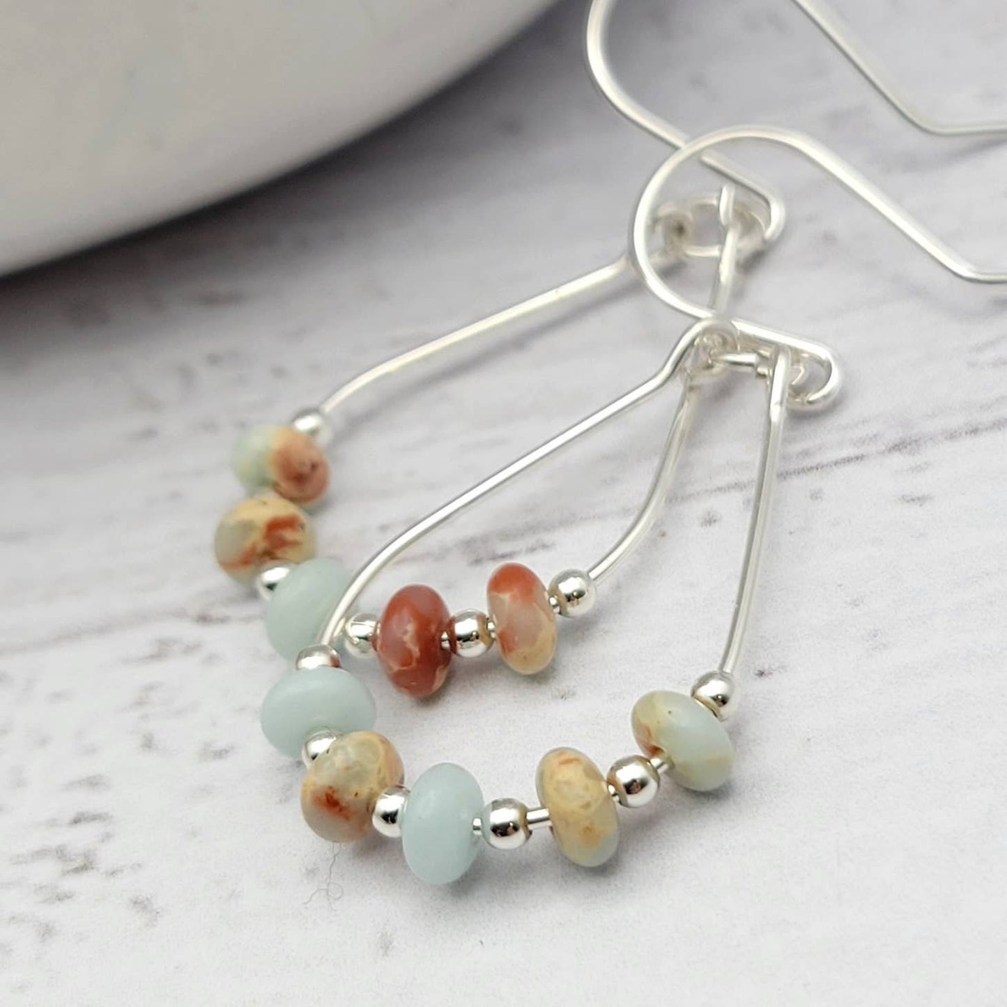 Light Blue Jasper Sterling Silver Earrings featuring handmade amazonite teardrop hoops designed for women who love elegant, natural blue jewelry. These artisanal earrings blend soothing jasper and amazonite stones with sterling silver craftsmanship, creating a delicate yet eye-catching accessory. Perfect as a gift for her or a bridesmaid gift, they add a calming, stylish touch to any outfit, ideal for everyday wear or special occasions with a boho-chic flair.