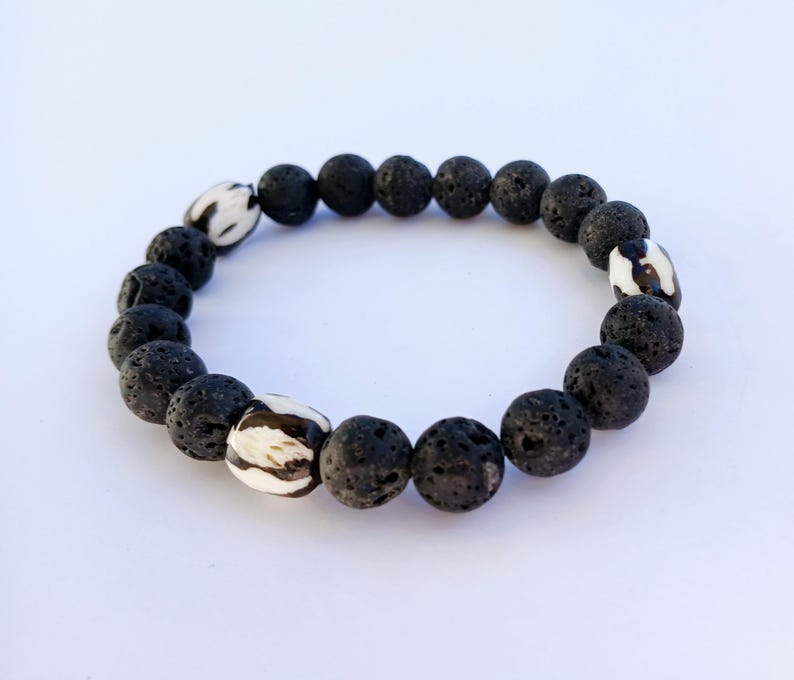 Tibetan Bone Bracelet with 12mm black lava stone beads, designed as a stretch diffuser bracelet for meditation and grounding. This handmade men’s bracelet combines traditional Tibetan jewelry elements with natural lava stones, perfect for essential oils. A meaningful lucky charm and spiritual accessory, ideal for promoting calm and focus. Great handmade gift for him—perfect for yoga, wellness, or daily wear with intention and style.