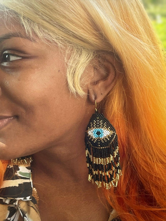 Mystical Eye Seed Bead Fringe Earrings featuring intricate handmade tribal designs with colorful seed bead fringes. These unique boho statement earrings offer bold dangles that capture attention with their vibrant colors and artistic craftsmanship. Perfect for women who love expressive, culturally inspired jewelry, they make an ideal gift for festivals, special occasions, or everyday wear. Lightweight and eye-catching, these earrings add a free-spirited, mystical touch to any outfit.