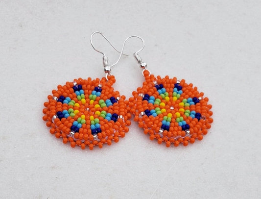 Orange Native Beaded Earrings featuring vibrant southwestern-style sunburst design with colorful beads arranged in a bold, retro boho pattern. These handmade statement earrings are perfect for women who love artisanal jewelry with cultural flair and eye-catching color. Ideal for festivals, casual wear, or special occasions, adding a lively pop of orange and warm tones to any outfit. A unique handmade gift that celebrates heritage and bold style.