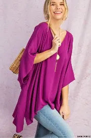 Purple V-neck drop shoulder tunic for women featuring a poncho-style design with side slits and a high-low hem. Made from soft, breathable rayon fabric, this comfortable and casual chic top offers a relaxed fit ideal for everyday wear. The versatile silhouette combines style and ease, making it perfect for layering or wearing on its own during warmer seasons or transitional weather.