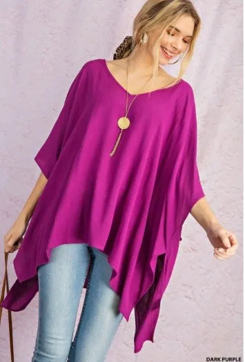 Purple V-neck drop shoulder tunic for women featuring a poncho-style design with side slits and a high-low hem. Made from soft, breathable rayon fabric, this comfortable and casual chic top offers a relaxed fit ideal for everyday wear. The versatile silhouette combines style and ease, making it perfect for layering or wearing on its own during warmer seasons or transitional weather.