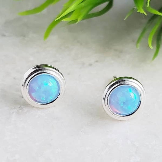 "Fire Opal Stud Earrings featuring vibrant azure blue bezel settings, crafted in high-quality sterling silver. These tiny, dainty earrings are perfect for women and girls who love minimalist yet elegant jewelry. The opal stones reflect fiery hues, adding a touch of sparkle and charm to any outfit. Ideal as a thoughtful gift for birthdays, anniversaries, or special occasions. A beautiful piece of opal jewelry for everyday wear or special events.